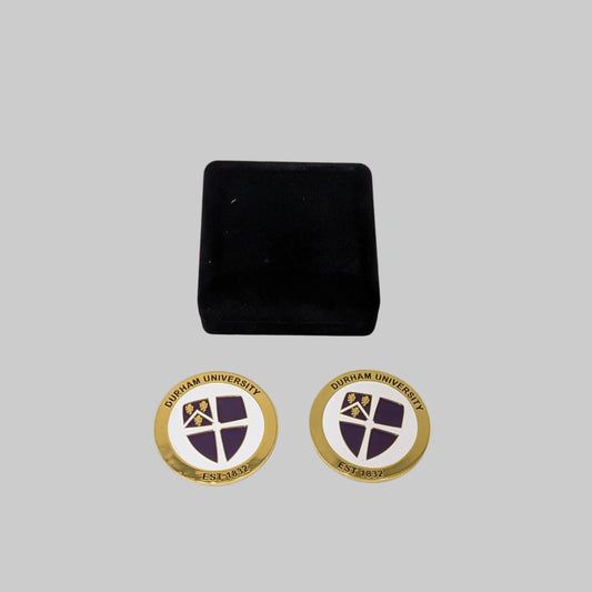 Durham University commemorative coin, gold round the outside with 'Durham University' in black around the top of the coin and est. 1832 along the bottom. Featuring a purple university crest on a white background in the centre. Same design on each side, coin comes presented in a black velvet gift box.