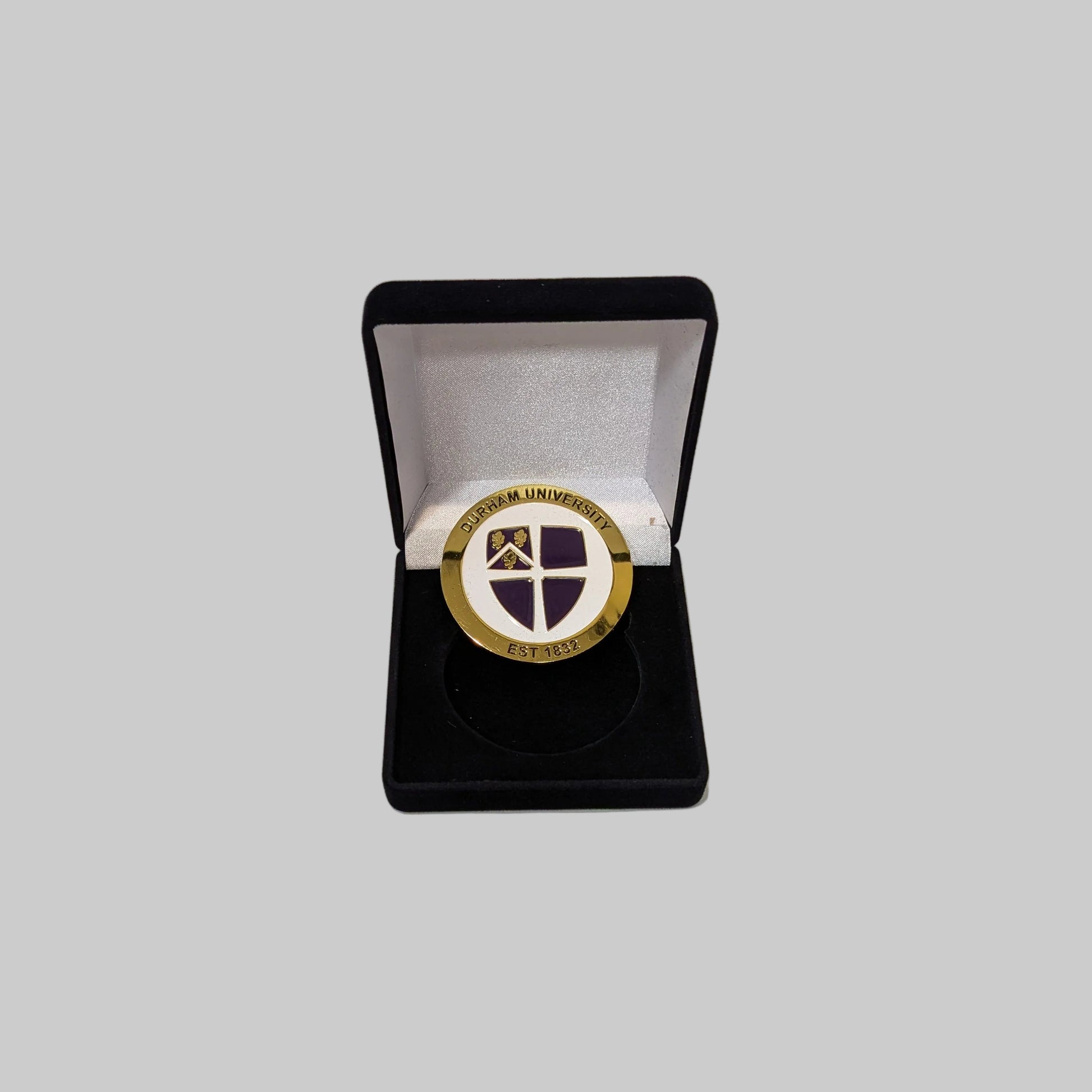 Durham University commemorative coin, gold round the outside with 'Durham University' test and est. 1832. Featuring a purple university crest on a white background. Same design on each side, coin comes presented in a black gift box.